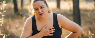 A woman walking outdoors, looking like she's in pain and out of breath.