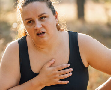 A woman walking outdoors, looking like she's in pain and out of breath.