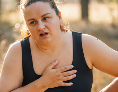 A woman walking outdoors, looking like she's in pain and out of breath.
