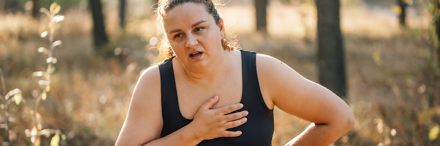 A woman walking outdoors, looking like she's in pain and out of breath.