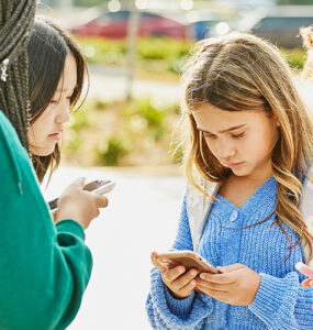 A group of teenage students standing outside school, using their cell phones.