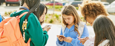 A group of teenage students standing outside school, using their cell phones.