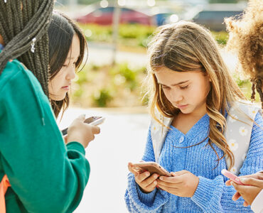 A group of teenage students standing outside school, using their cell phones.