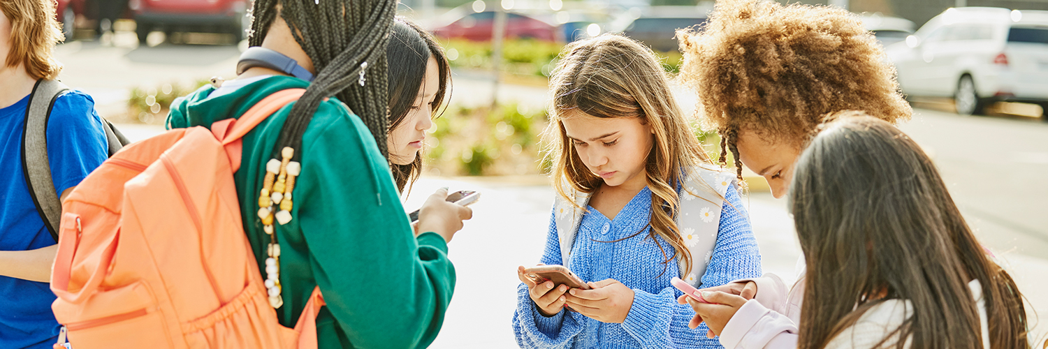 A group of teenage students standing outside school, using their cell phones.