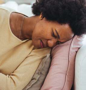 A woman laying on her couch, holding her stomach in pain.