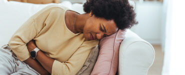 A woman laying on her couch, holding her stomach in pain.