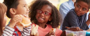 Kids sitting in the school cafeteria, eating lunch together.