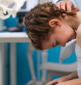 A girl having her spine examined for scoliosis by a orthopedist in a medical office.