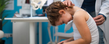 A girl having her spine examined for scoliosis by a orthopedist in a medical office.