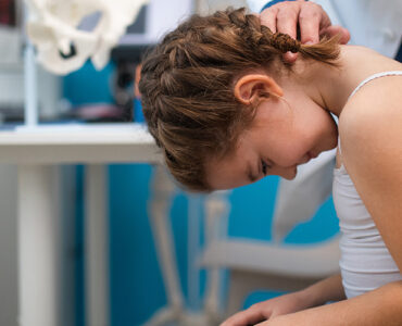 A girl having her spine examined for scoliosis by a orthopedist in a medical office.
