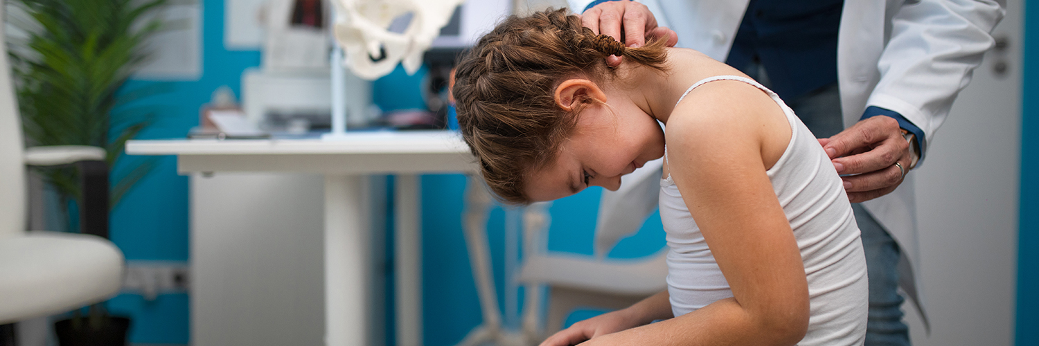 A girl having her spine examined for scoliosis by a orthopedist in a medical office.