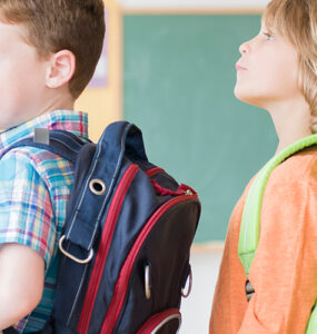 A group of elementary aged students standing in line at school, wearing their backpacks.