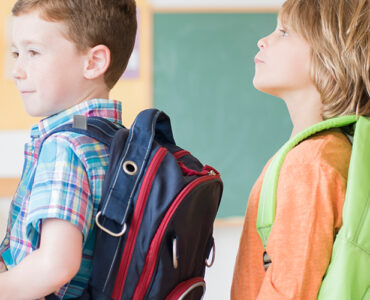 A group of elementary aged students standing in line at school, wearing their backpacks.