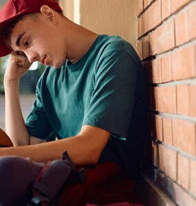Boy sitting in high school. hallway, with his head down and holding a basketball.