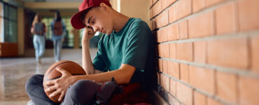 Boy sitting in high school. hallway, with his head down and holding a basketball.