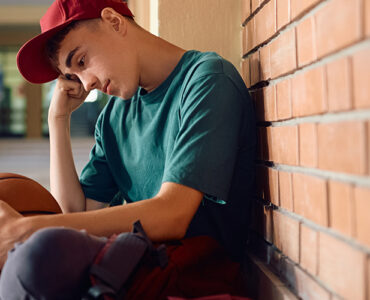 Boy sitting in high school. hallway, with his head down and holding a basketball.
