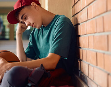 Boy sitting in high school. hallway, with his head down and holding a basketball.