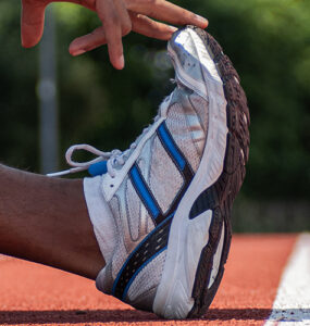 An up close image of a man's foot with his hand stretching it, while standing on a sports track.