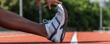 An up close image of a man's foot with his hand stretching it, while standing on a sports track.