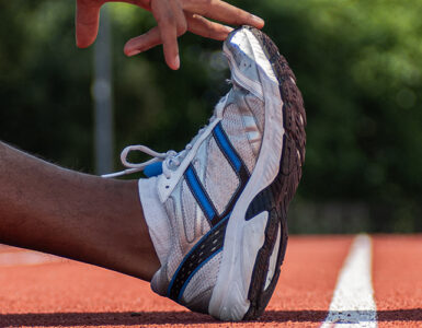 An up close image of a man's foot with his hand stretching it, while standing on a sports track.