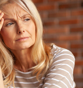 A middle-aged woman with her hand to her forehead, looking run down and tired.