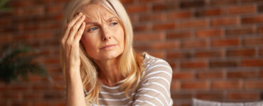 A middle-aged woman with her hand to her forehead, looking run down and tired.