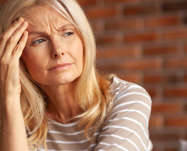 A middle-aged woman with her hand to her forehead, looking run down and tired.