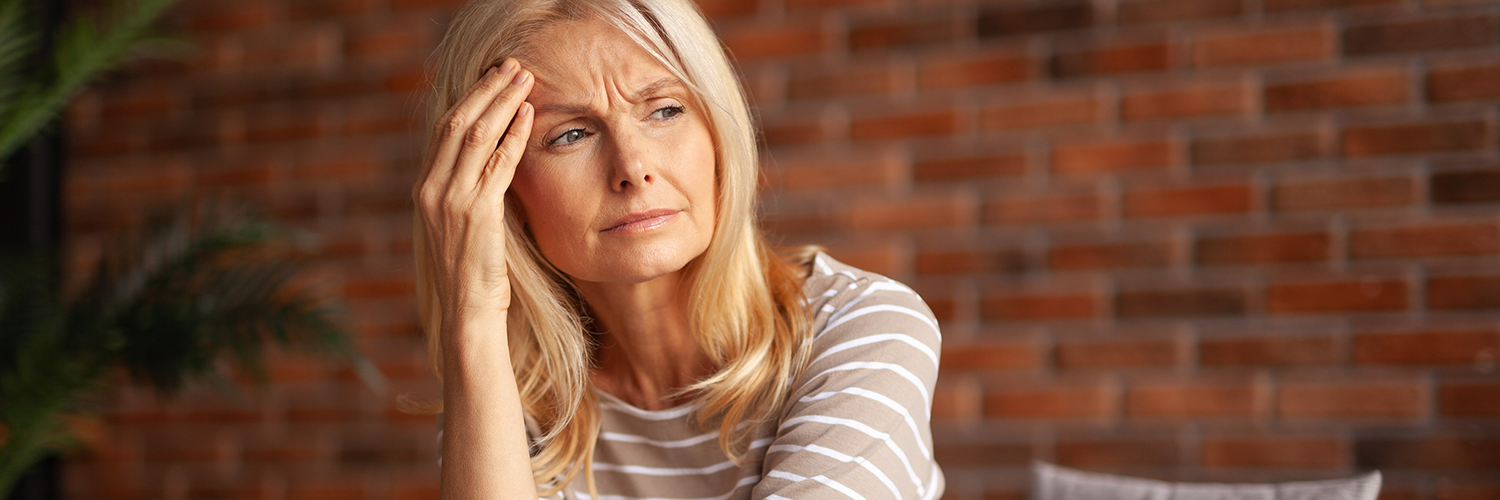 A middle-aged woman with her hand to her forehead, looking run down and tired.