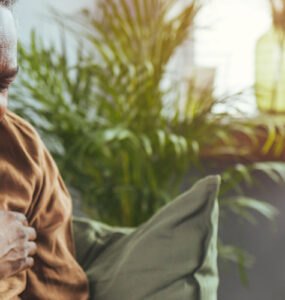 An older man sitting on his couch, clutching his chest in pain.