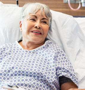 An older woman laying in a hospital bed, speaking to her doctor while smiling.
