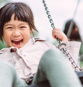 A young girl outside on a swing, with a huge smile on her face.