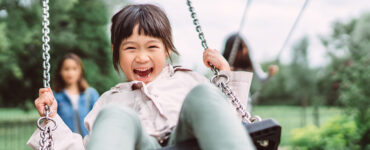 A young girl outside on a swing, with a huge smile on her face.