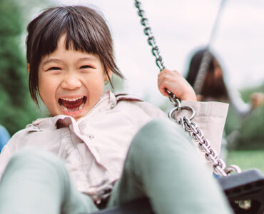 A young girl outside on a swing, with a huge smile on her face.