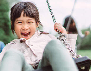 A young girl outside on a swing, with a huge smile on her face.