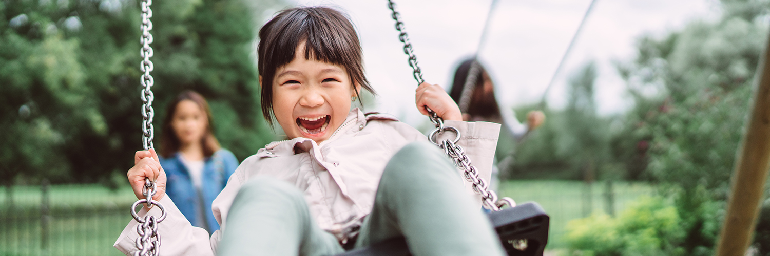 A young girl outside on a swing, with a huge smile on her face.