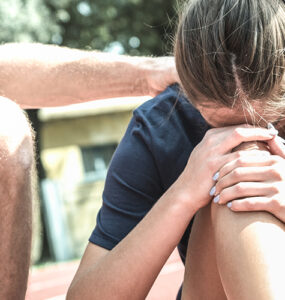 A female athlete who is on the floor, grabbing her leg in pain, with her coach helping her.