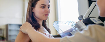 A woman getting a mammogram, with the radiologists hand on her shoulder, reassuring her.