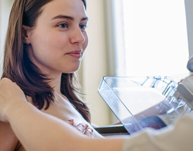 A woman getting a mammogram, with the radiologists hand on her shoulder, reassuring her.