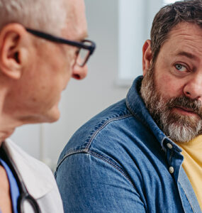 An overweight and middle-aged man sitting with his doctor to review his medical report.