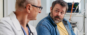 An overweight and middle-aged man sitting with his doctor to review his medical report.
