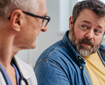 An overweight and middle-aged man sitting with his doctor to review his medical report.