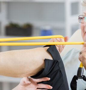 A senior woman stretching her leg alongside her female physical therapist.