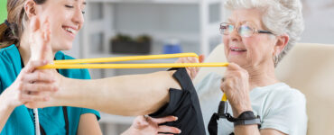 A senior woman stretching her leg alongside her female physical therapist.