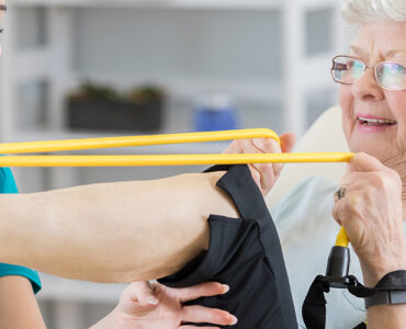 A senior woman stretching her leg alongside her female physical therapist.