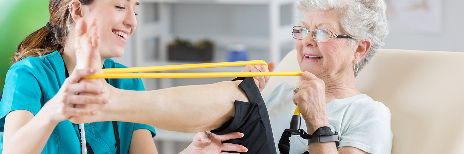 A senior woman stretching her leg alongside her female physical therapist.