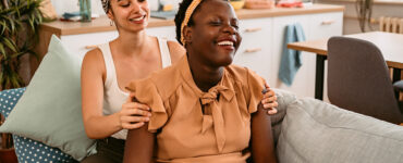 A pregnant woman sitting on her couch, having her shoulders rubbed by her birth doula.