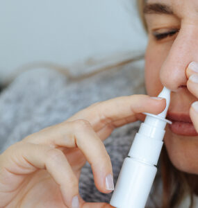 A young women on her couch, using a nasal stick for decongesting her nose.