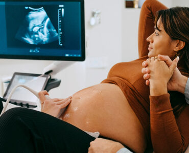 A pregnant woman holding her husband's hand while getting an ultrasound.