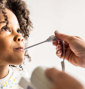 A young girl at a doctor's office, having her temperature taken while looking at the physician's face.