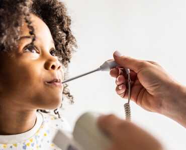 A young girl at a doctor's office, having her temperature taken while looking at the physician's face.